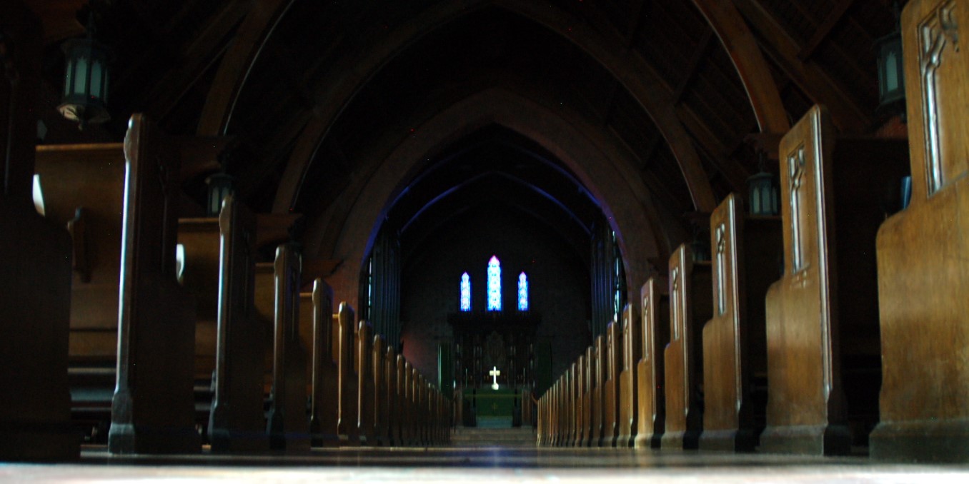 inside darkened church sitting on floor looking the length of the nave and chancel to altar and reredos