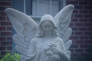 concrete angel statue in front of brick building with window
