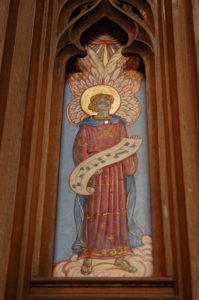 A painting of an angel holding sheet music. Part of the reredos, or carving above/behind the high altar