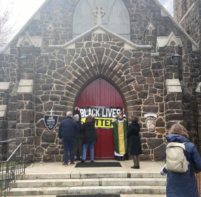 people hanging Black Lives Matter banner on front doors of dark sandstone church