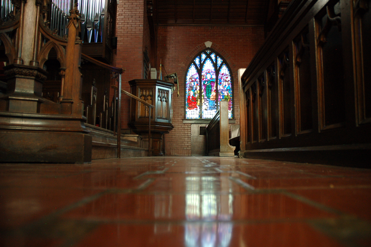 view of pulpit, stained glass window, and front pew with light reflecting through window onto polished brick floor