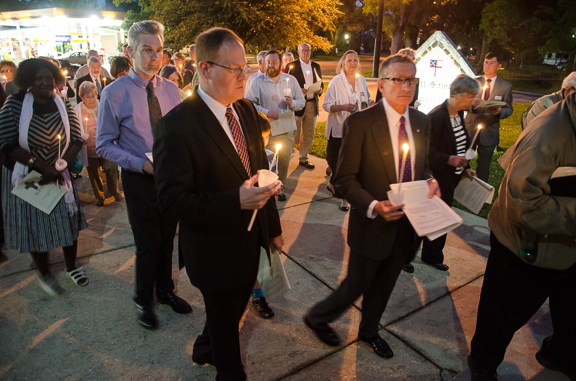 people holding candles on sidewalk in front of church