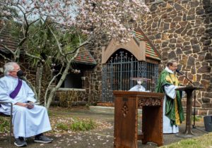two priests with table holding eucharist/communion elements, in a church garden