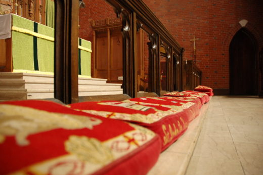 View from near the floor of a church altar rail with cushioned kneelers along it. Stone steps and an altar are visible to one side.