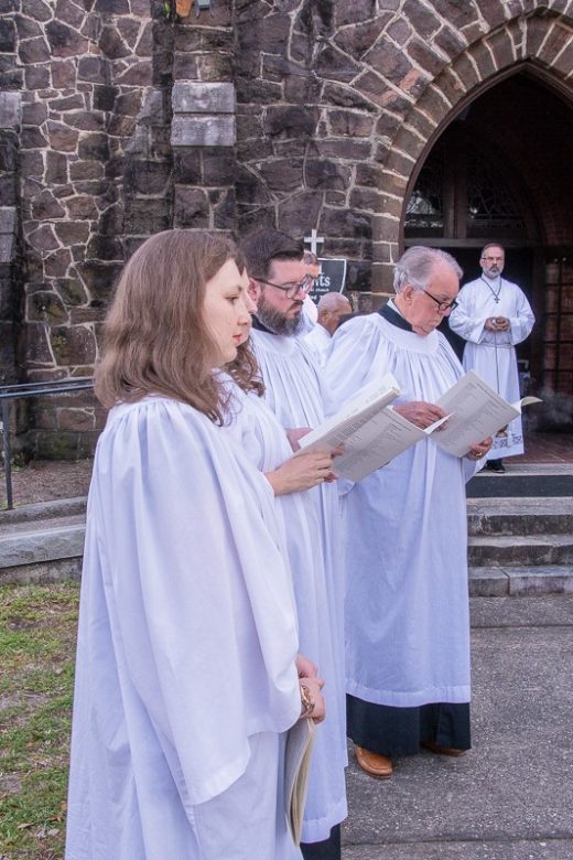 Choristers in front of a stone-faced church with its doors open