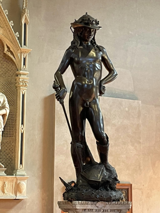 bronze statue of a naked young man standing on the helmeted head of his enemy
