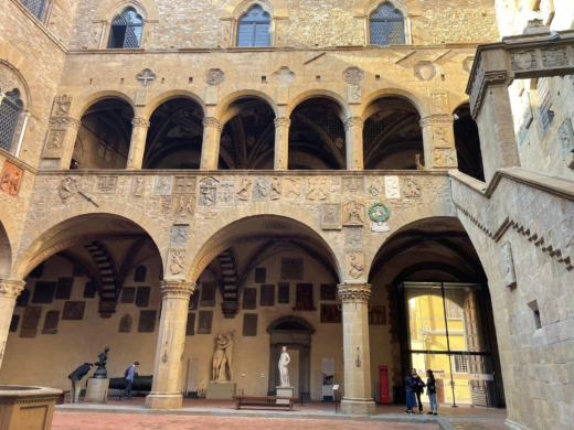 a stone building with a groin-vaulted arcaded walkway, containing plaques on the walls and statuary below