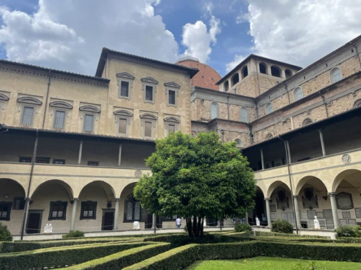 in the cloister of an ancient church, with grass, bushes, and a small tree in the middle