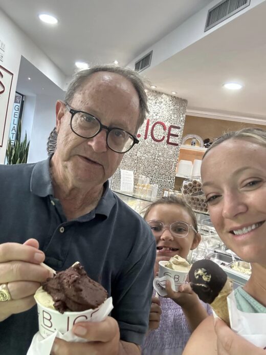 two adults and a child pose with their food selections in a gelato shop in Italy